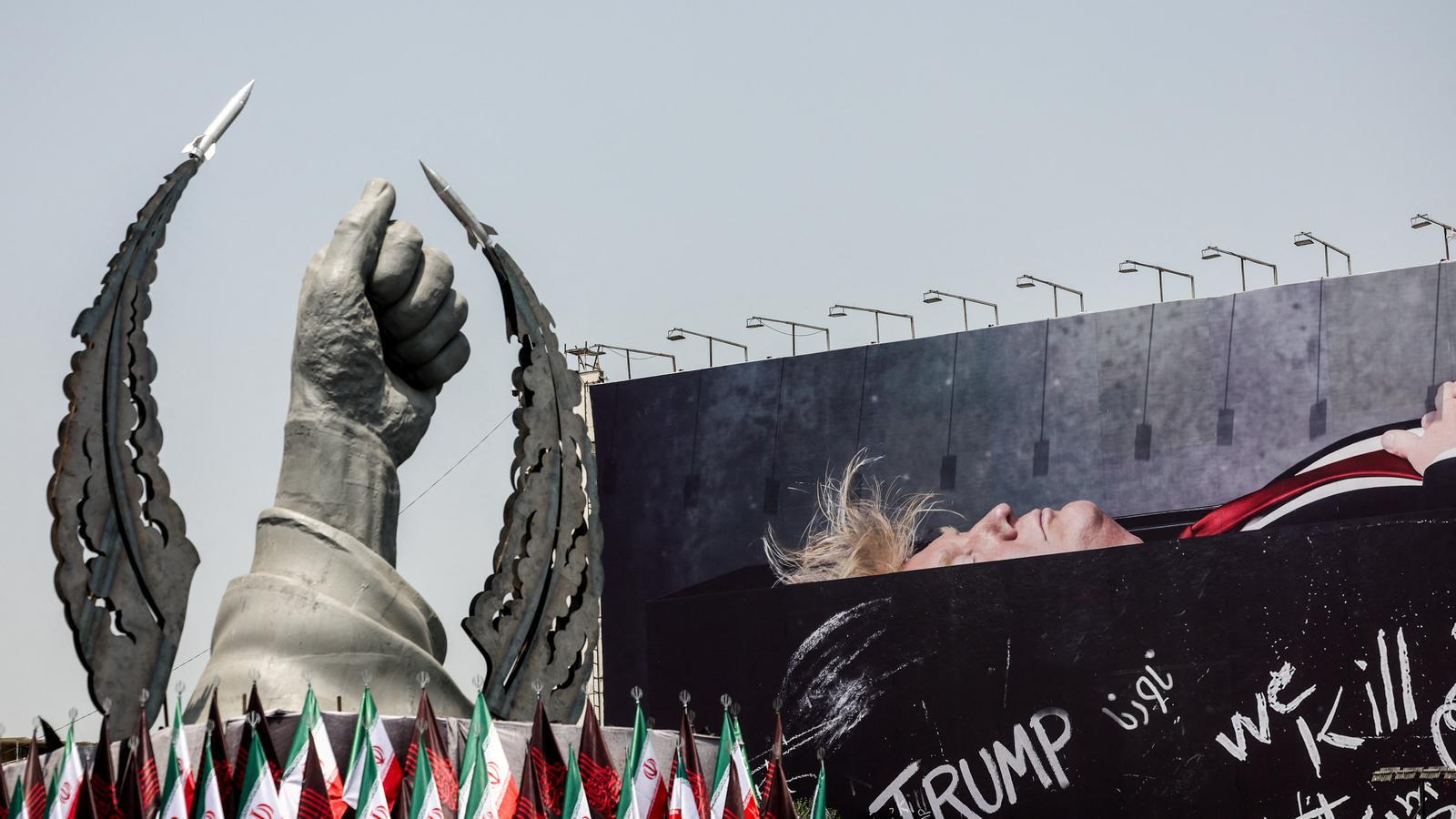 Una estatua que simboliza la mano del difunto líder supremo de Irán, el ayatolá Alí Jamenei, junto a un cartel de propaganda que representa al presidente de los Estados Unidos, Donald Trump, en un ataúd, en el centro de Teherán.
