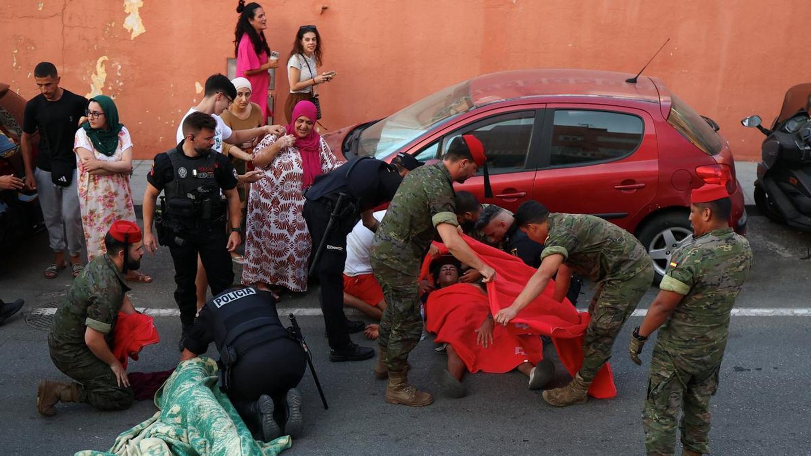 Policía y militares españoles atienden a migrantes heridos en una carretera, tras la travesía masiva a Ceuta.