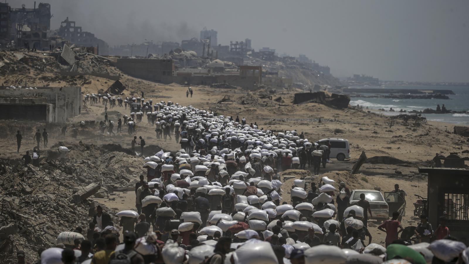 Displaced Palestinians carry bags of flour near a food distribution point in Zikim, in the northern Gaza Strip.
