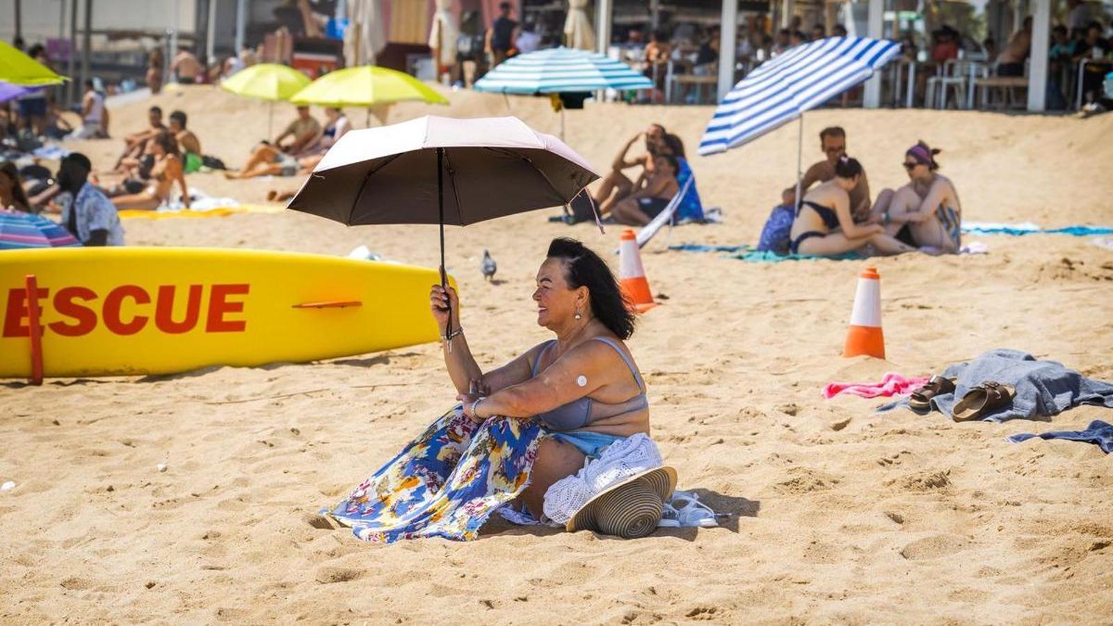 A woman protects herself from the sun with an umbrella on the Barceloneta beach.