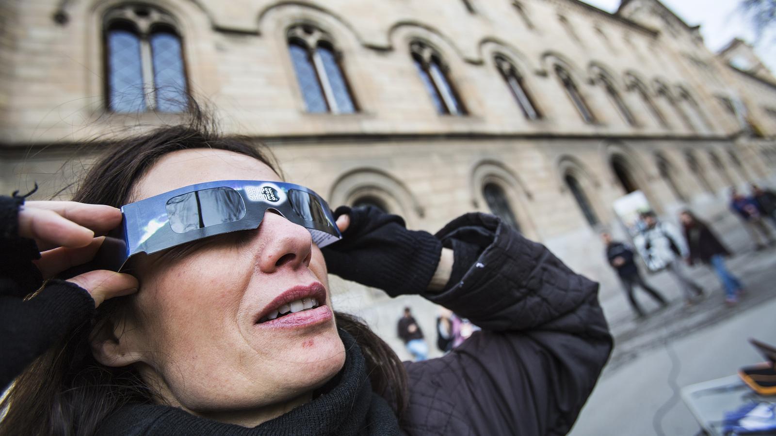 A woman tries on eclipse glasses in front of the University of Barcelona.