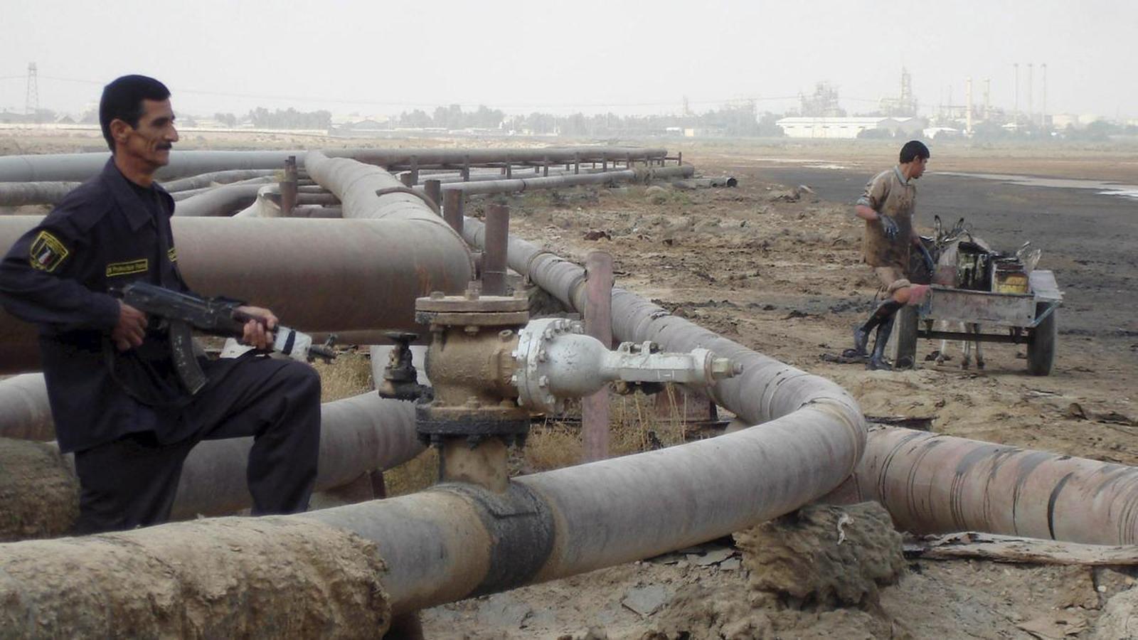 A security officer and a worker are working on a pipeline at a refinery in Baora, Iraq.