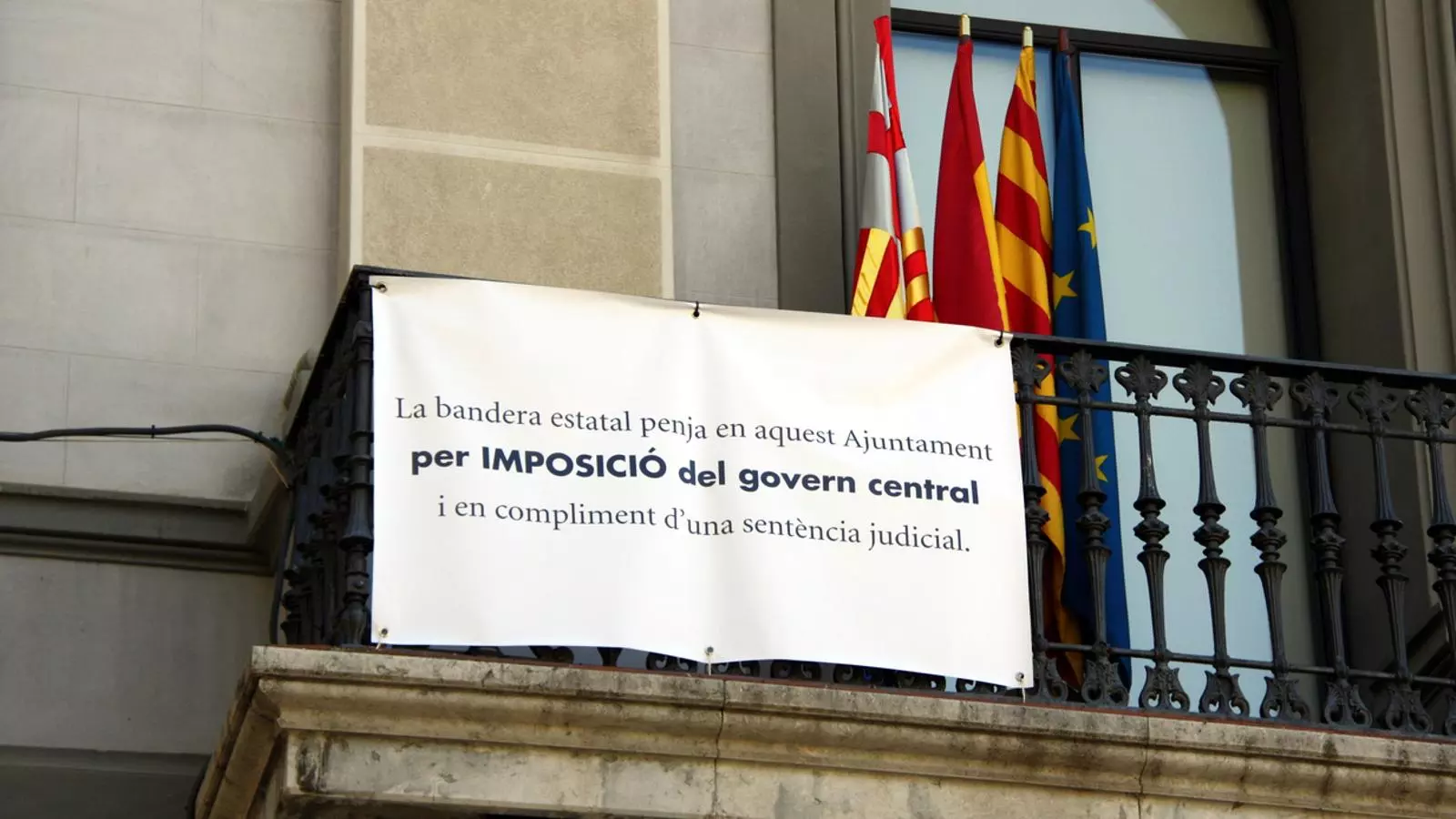 Detall del cartell on s'expliquen els motius pels quals l'Ajuntament d'Igualada ha penjat la bandera espanyola i, a darrere, les quatre banderes: la d'Igualada, l'espanyola, la catalana i l'europea / ACN