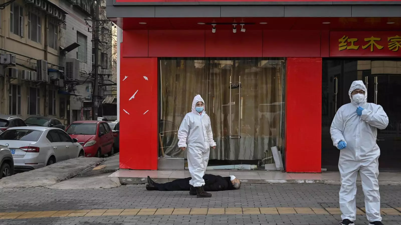 Funcionaris amb vestits de protecció al costat del cos d'un home gran amb mascareta, que va morir en un carrer prop d'un hospital de Wuhan.