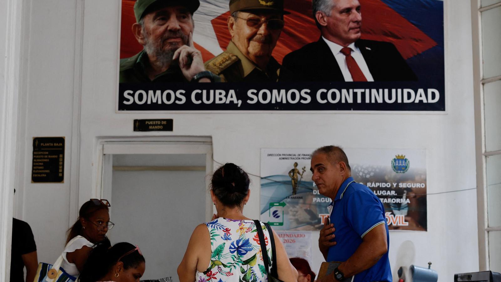 People in an office of the Ministry of Finance of Cuba under a poster of the deceased Cuban president Fidel Castro, his brother, former president Raul Castro and president Miguel Díaz-Canel.