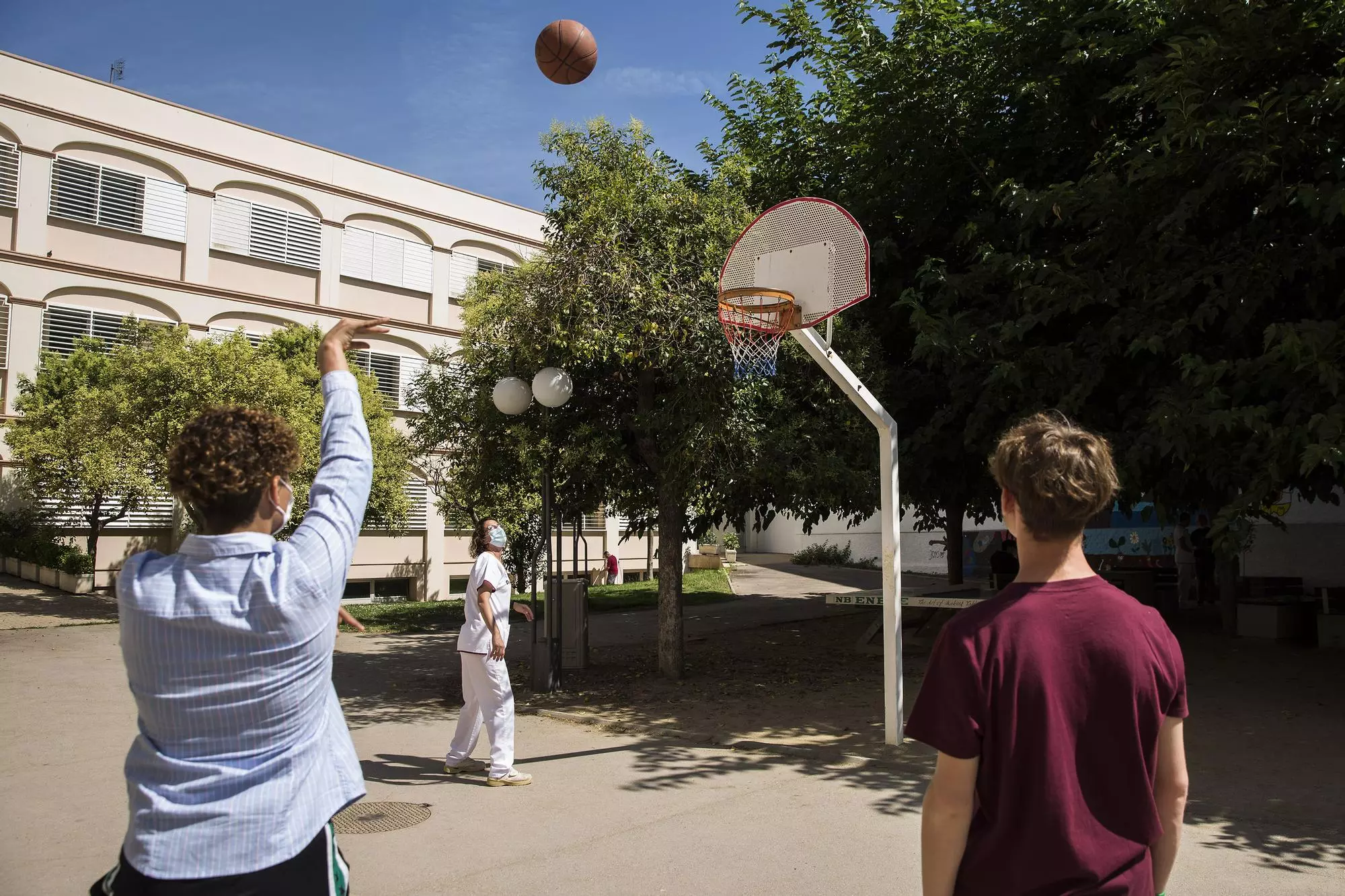Una infermera i dos pacients jugant a bàsquet al pati de la Unitat de Cures d’Adolescents del complex Benito Menni de Sant Boi