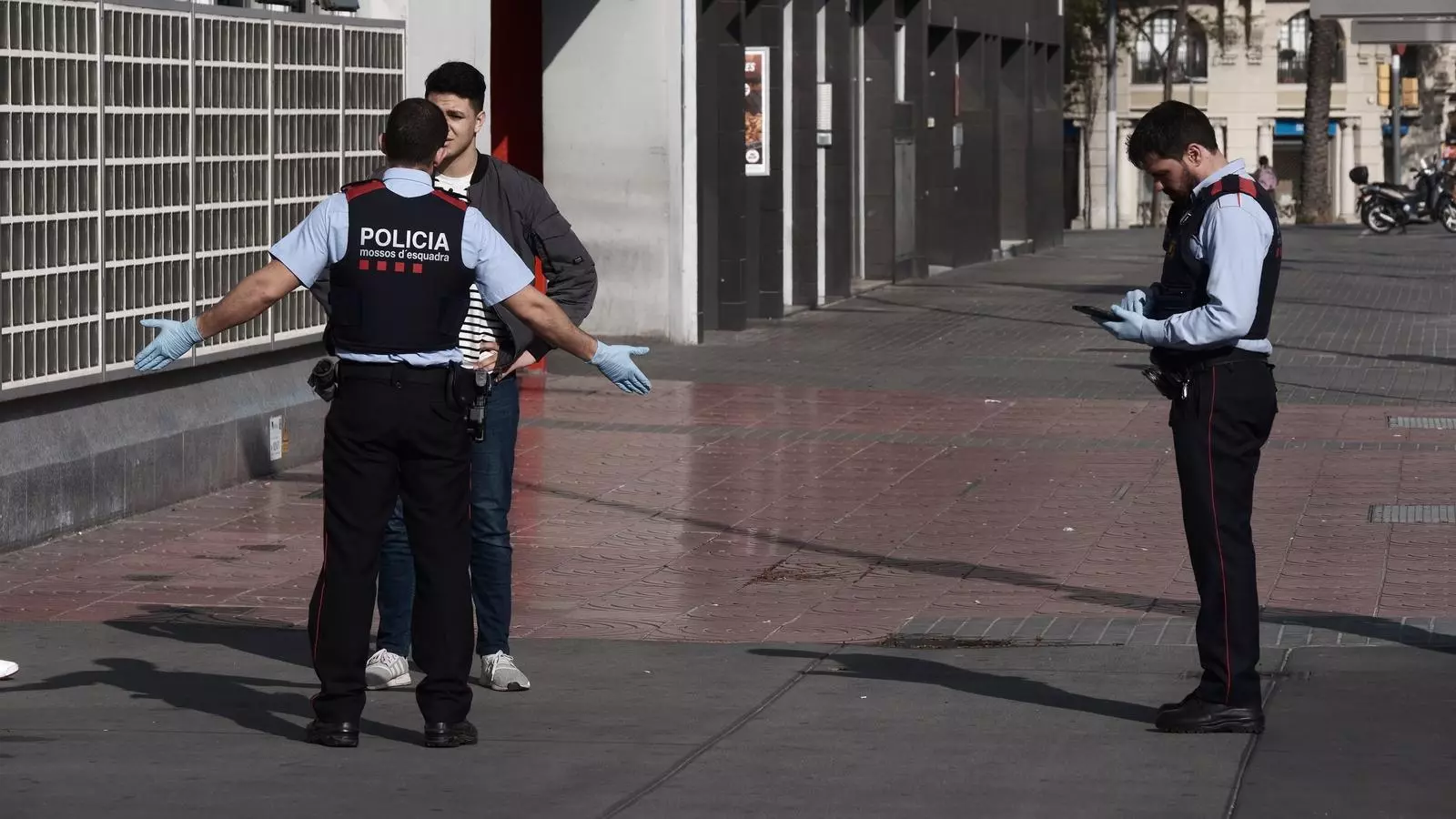 Dos agents dels Mossos comprovant aquest dilluns si un ciutadà que anava per la plaça Espanya de Barcelona compleix el confinament