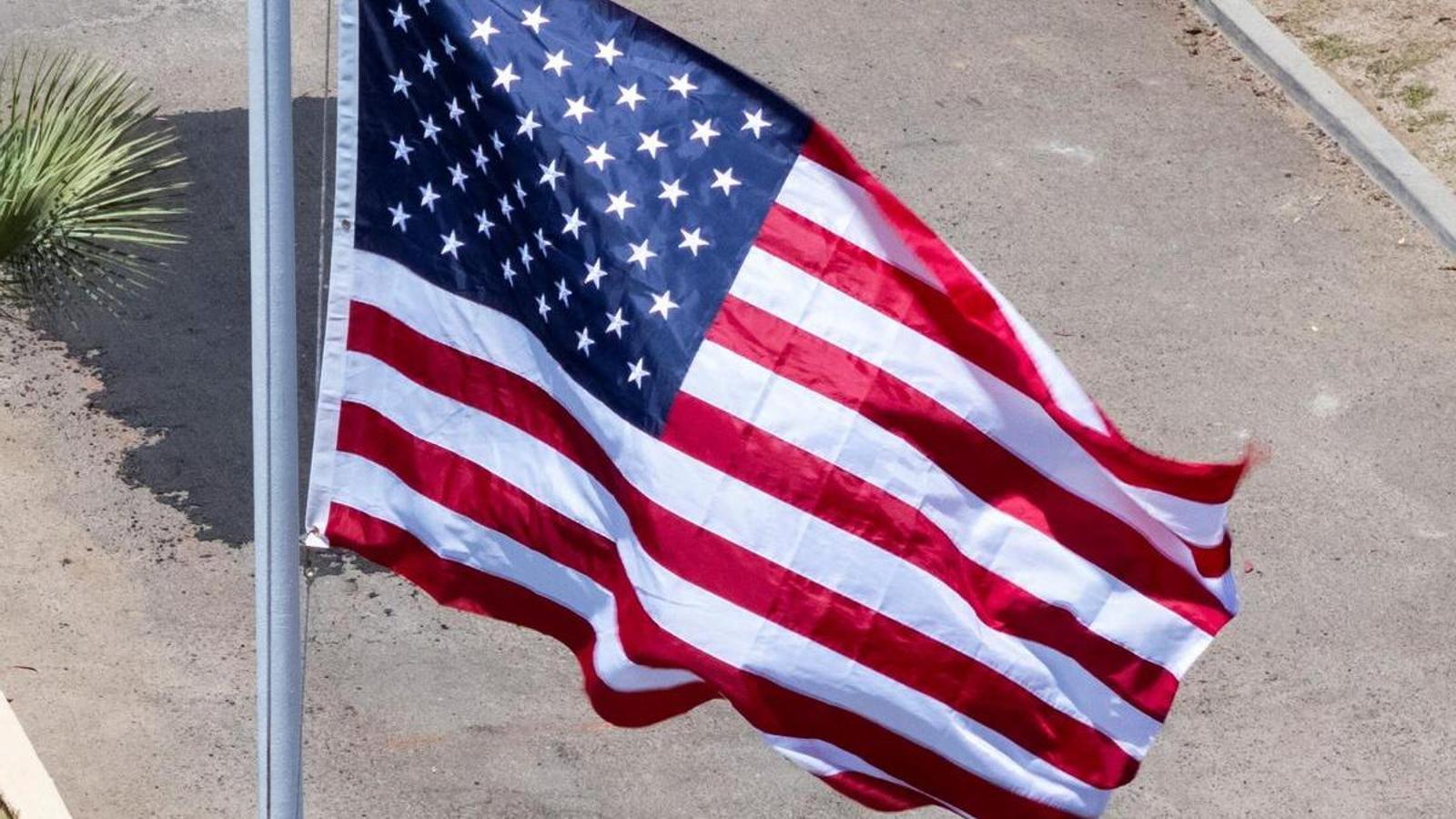 Una mujer vestida con chador debajo de una bandera de los Estados Unidos.