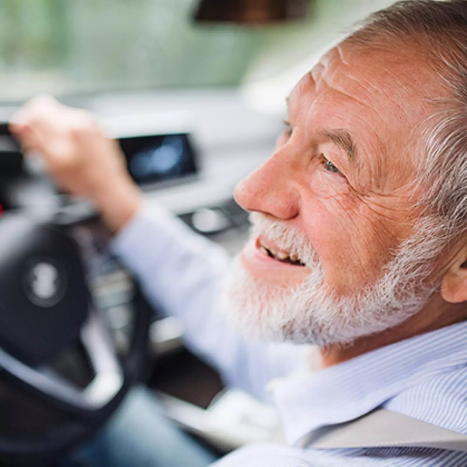 Close-up of happy senior man sitting in car in driver seat, driving.