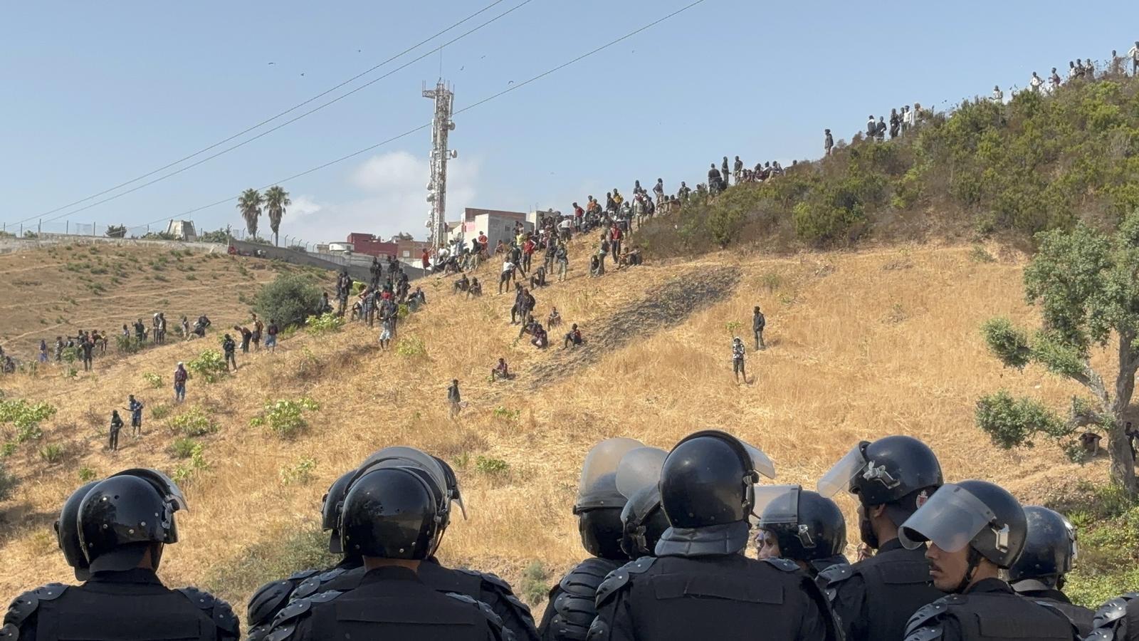 Moroccan police agents watch dozens of sub-Saharan men on a mountain next to Ceuta