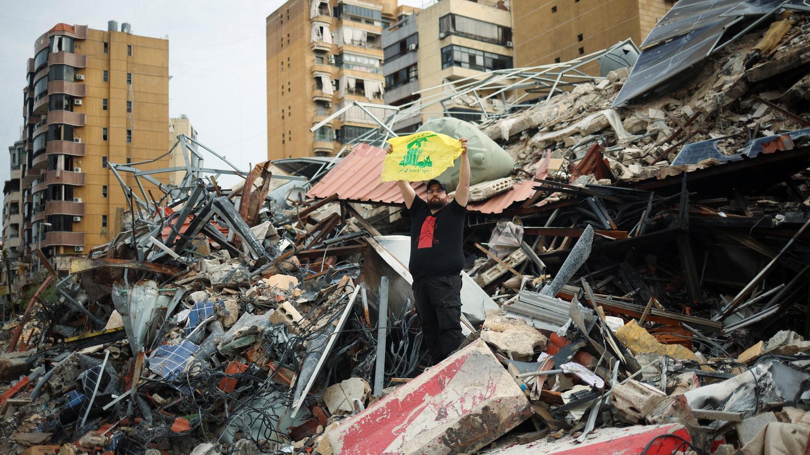 A man holds a Hezbollah flag while standing on the ruins of a damaged building, after a 10-day ceasefire between Lebanon and Israel came into effect, in the southern suburbs of Beirut, Lebanon, on April 17, 2026.