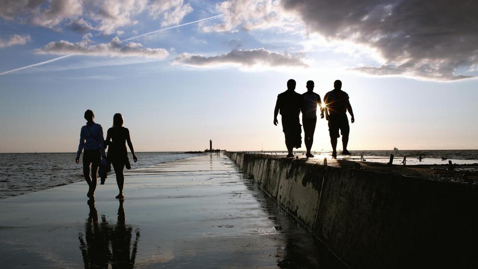 Un grupo de personas caminan cerca del mar en un paseo marítimo durante la salida del sol.