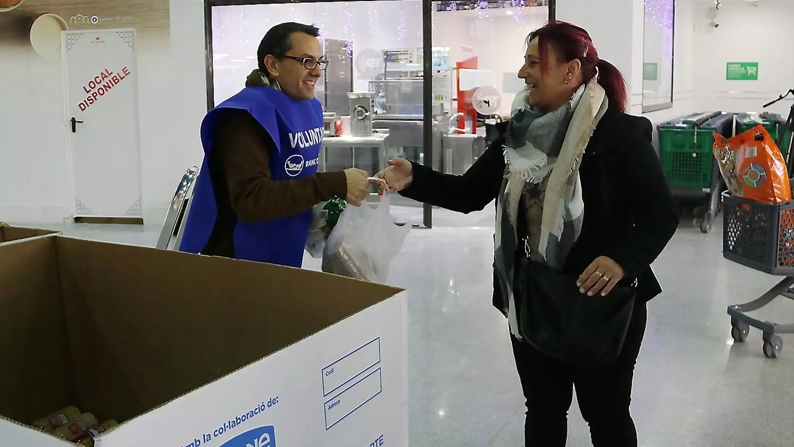 Una dona entregant menjar a un voluntari del Banc dels Aliments en un supermercat.