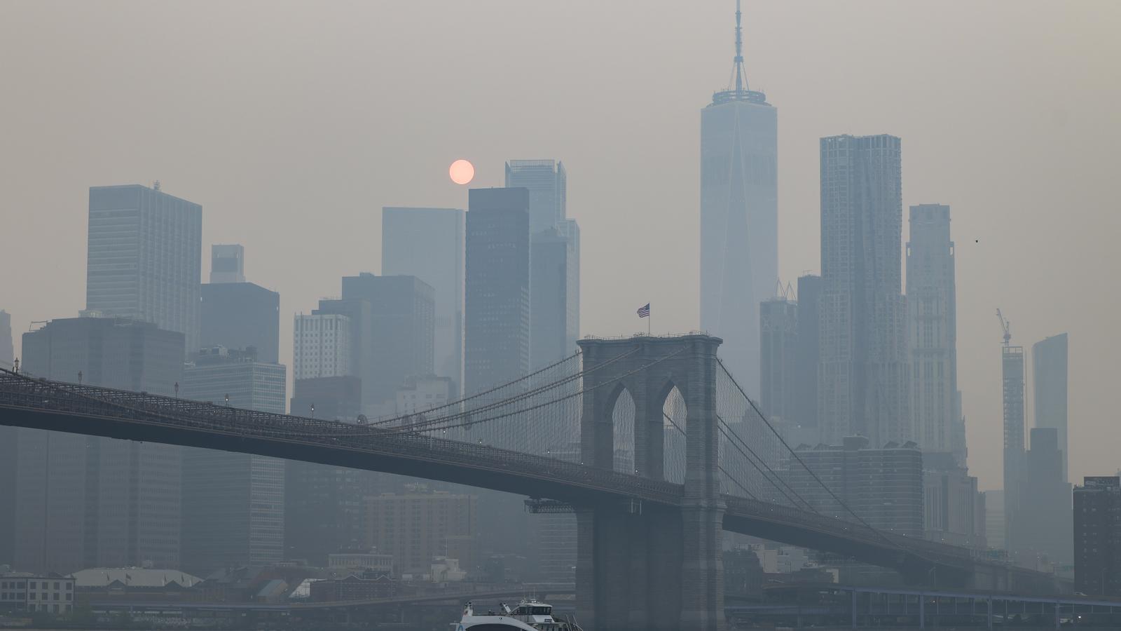 The smoke from the forest fires is seen between the Manhattan skyline and the Brooklyn Bridge from the Brooklyn promenade