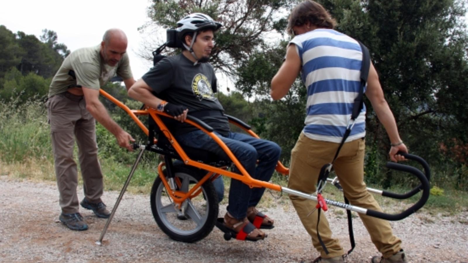 Una persona amb discapacitat fent ús de la cadira Joëlette, portada per dues persones al Parc Natural de Sant Llorenç de Munt