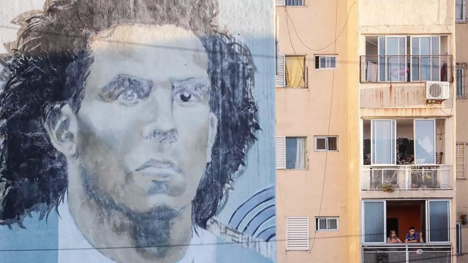 Uns nens mirant pel balcó de Fuerte Apache amb un mural de Carlos Tévez, el jugador nascut en aquest barri de Buenos Aires, en la quarantena obligatòria