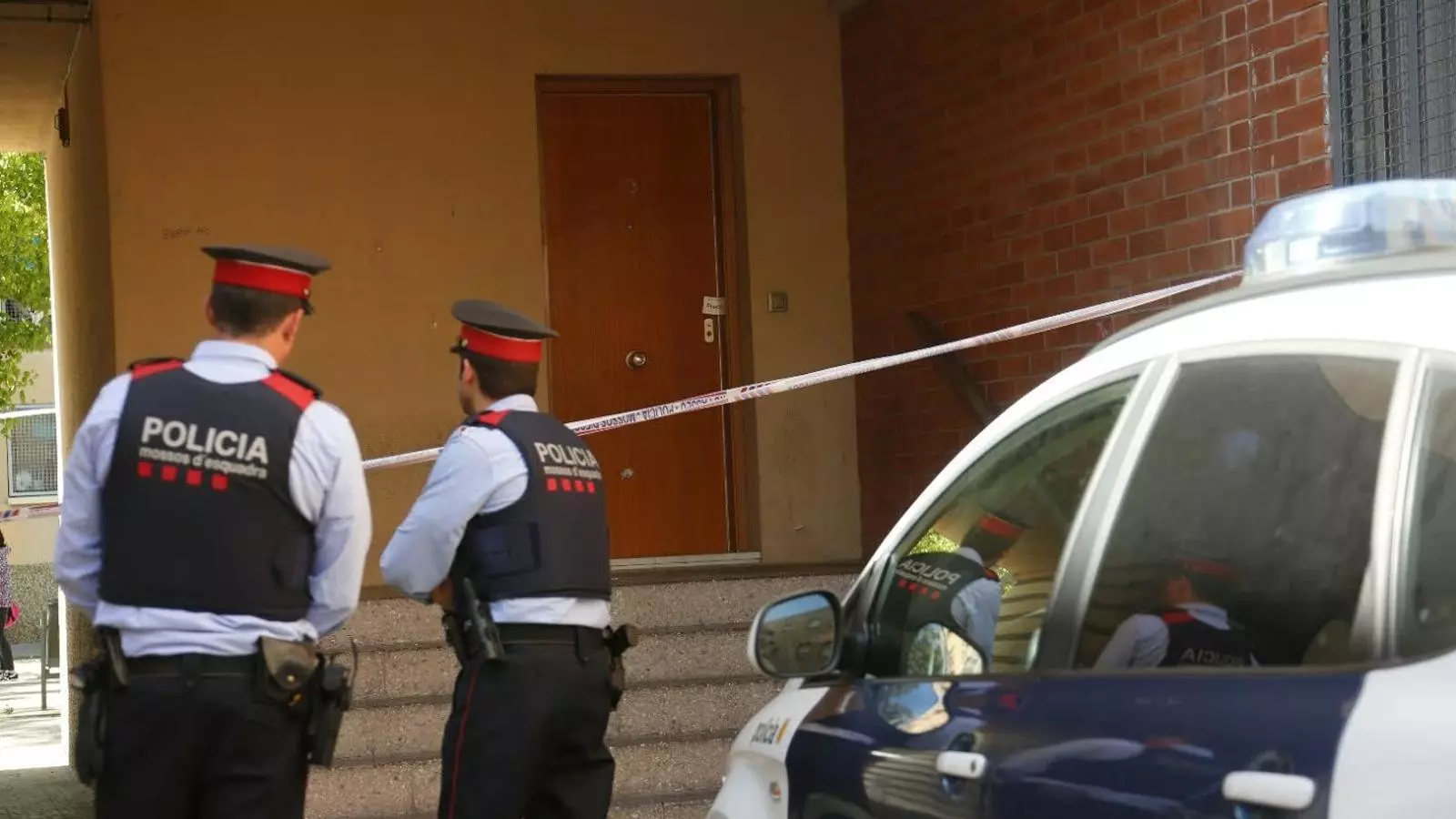Dos mossos d'esquadra al portal del pis del barri de Sant Cosme, al Prat de Llobregat, on aquest dijous hi van morir dues persones d'origen dominicà en la guerra entre bandes