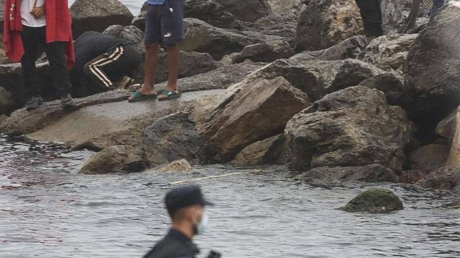 A national police officer watches an area where migrants settled in Ceuta are trying to fish for food.