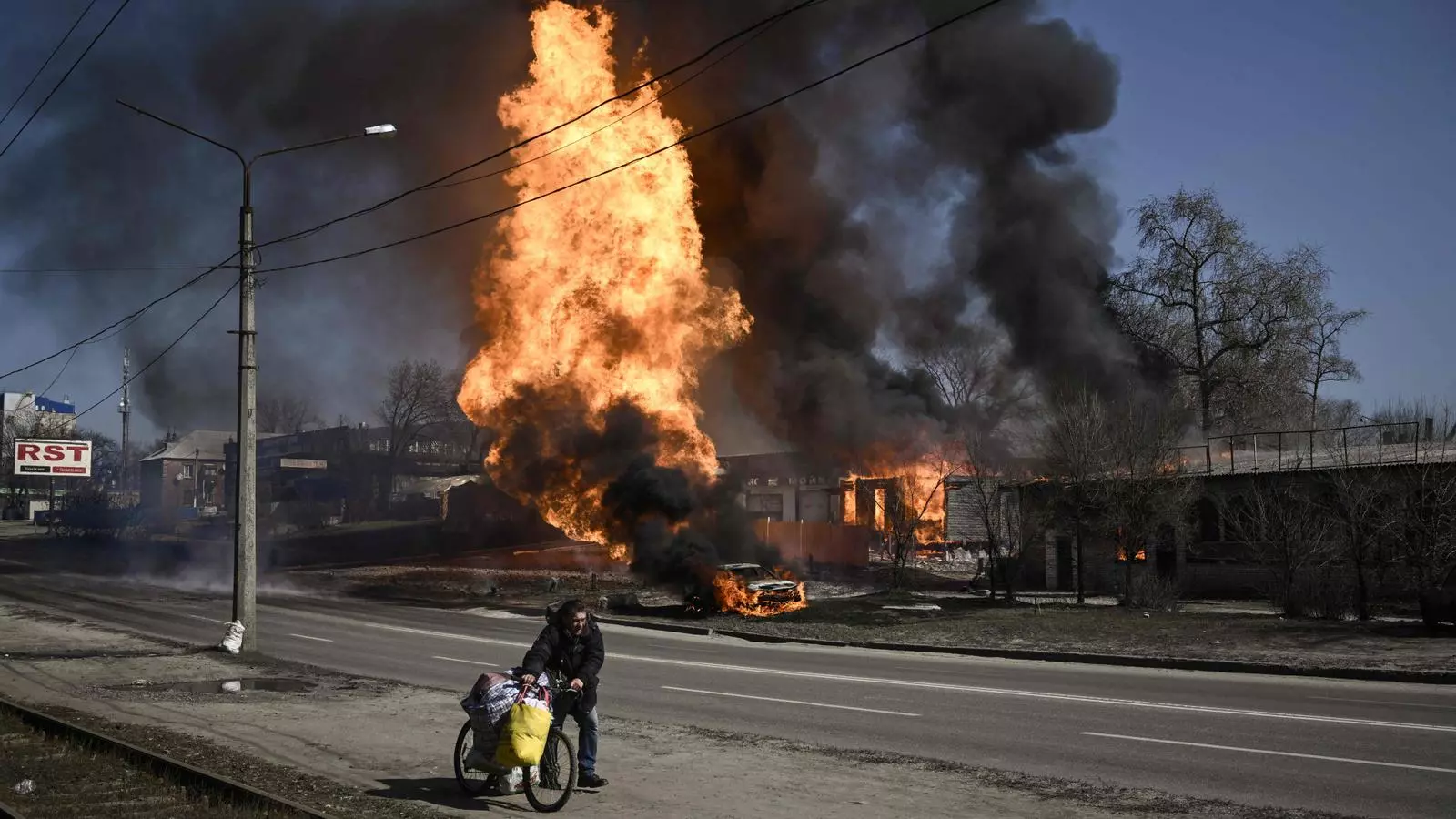Un hombre huye con sus pertenencias mientras el incendio traga un vehículo y un edificio en la ciudad Khàrkiv