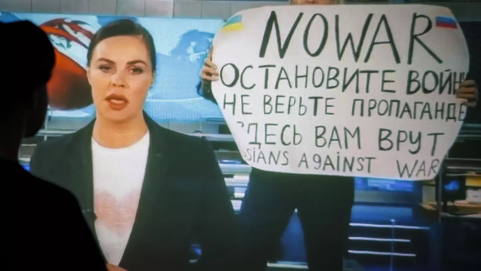 Una dona davant una pantalla on es projecta el moment en què Marina Ovsyannikova apareix a la televisió pública russa per protestar contra la guerra de Putin.