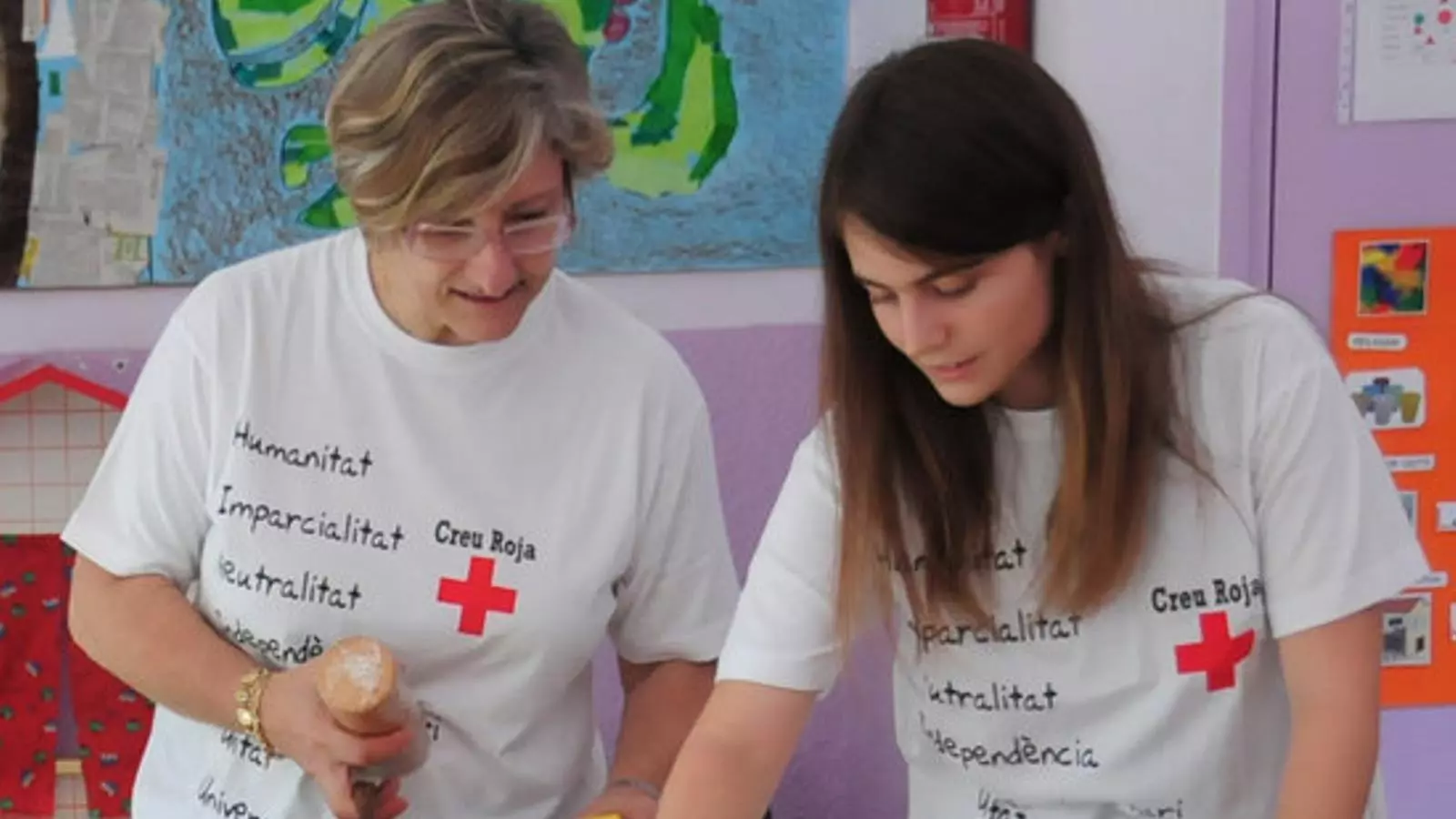 Dues voluntàries de la Creu Roja oferint aliments a nens amb risc d'exclusió social a les comarques gironines