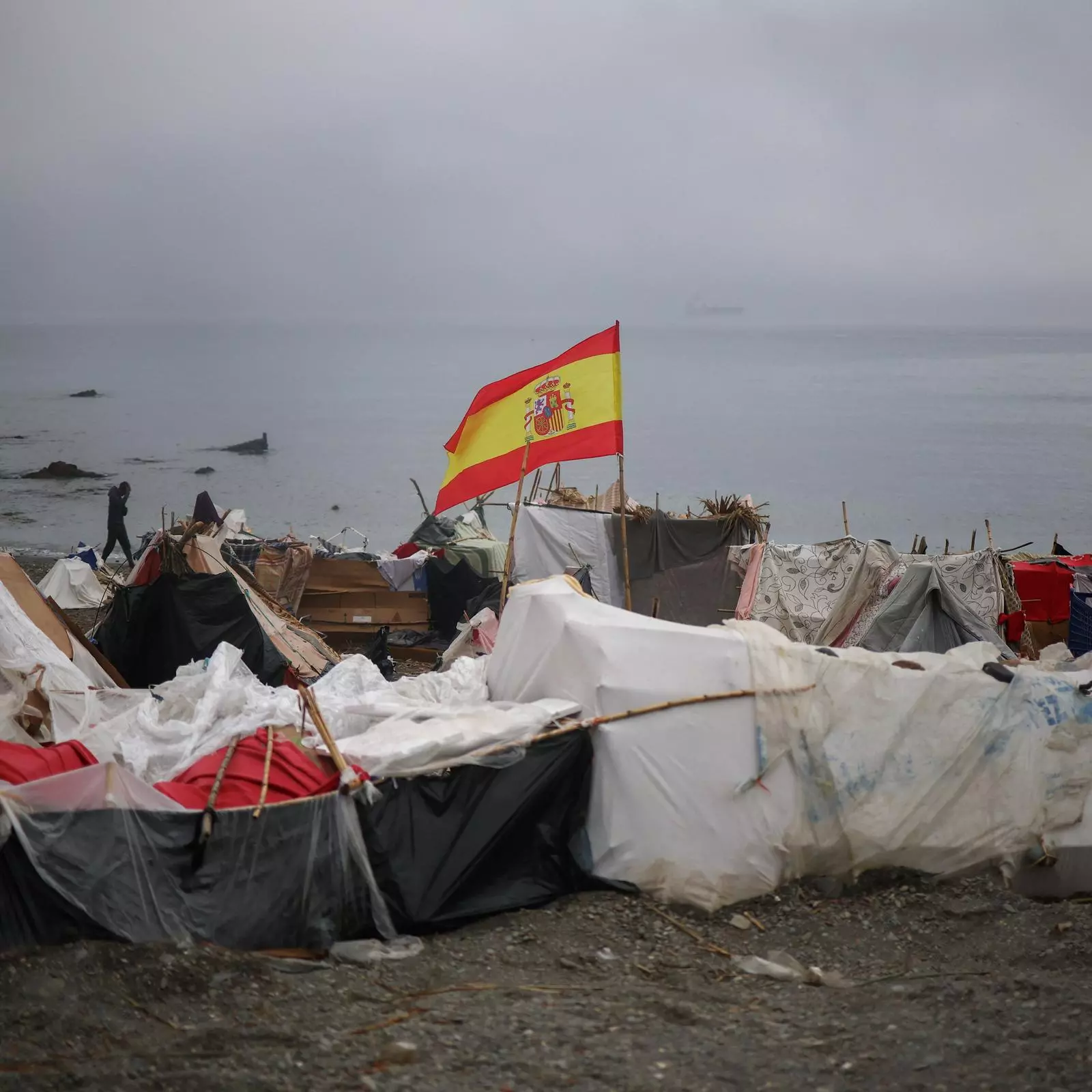 Una bandera española se erige sobre una de las tiendas del campamento improvisado situado en la playa del Trampolín, en Ceuta.
