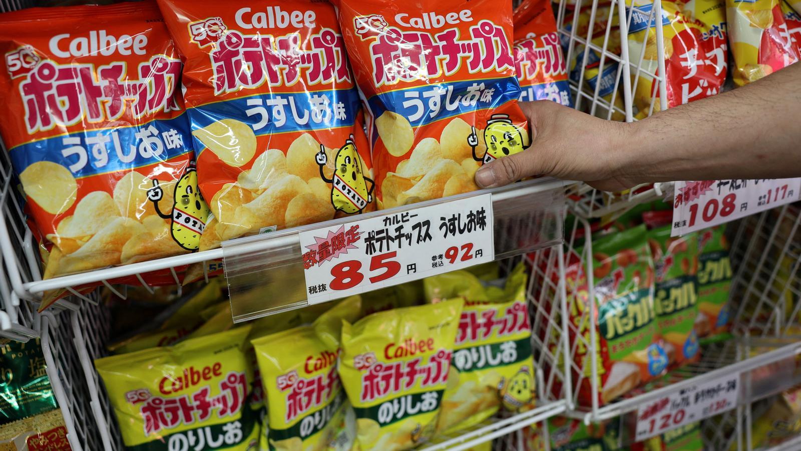 Un empleado repone bolsas de patatas fritas Calbee en un estante de una tienda especializada en golosinas y aperitivos en Tokio (Japón).