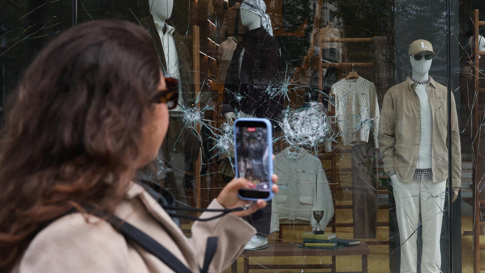 A woman photographs a shop window of a clothing chain establishment damaged by the riots in Paris.