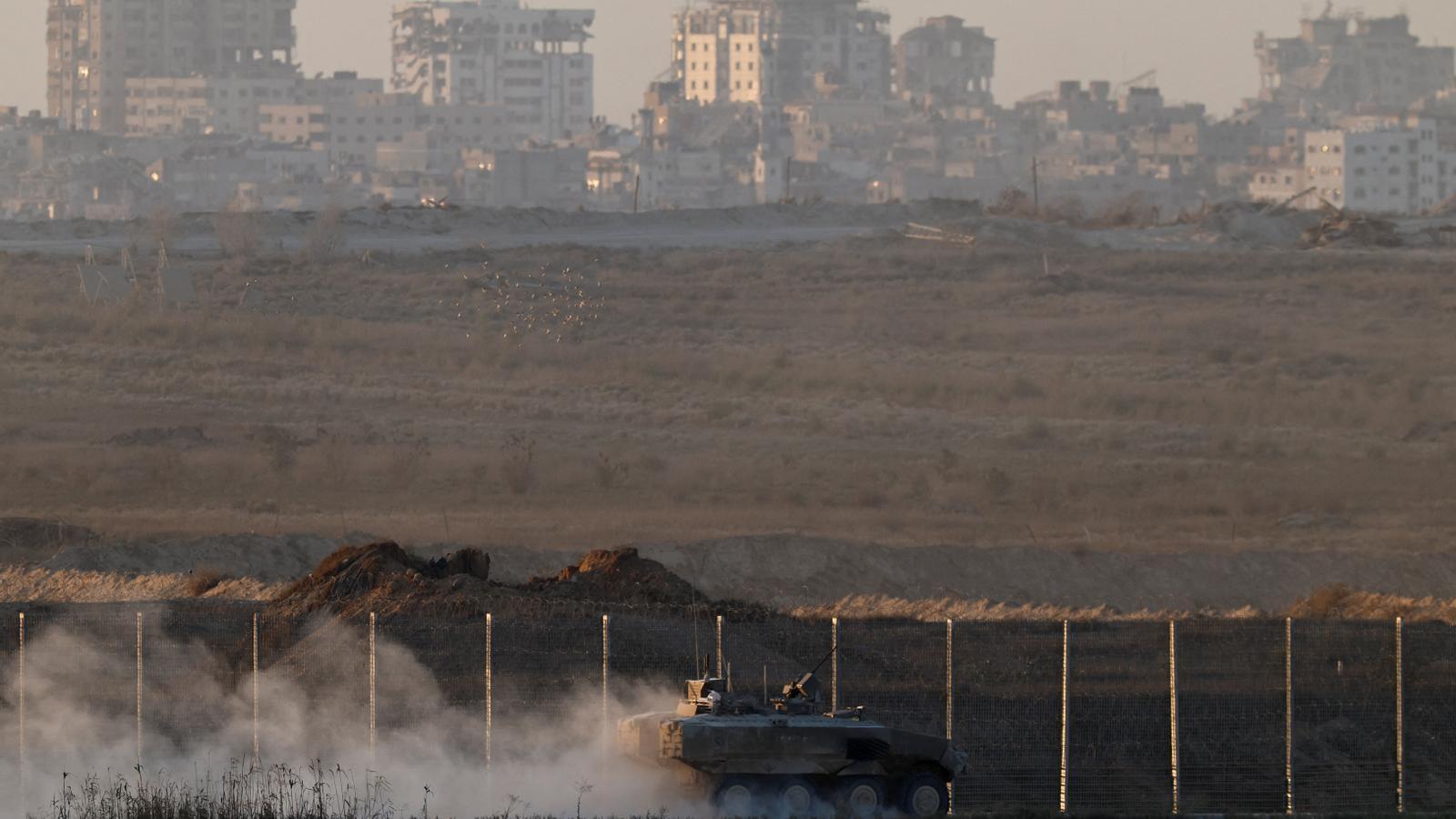 An Israeli armored vehicle maneuvers on the outskirts of the border with the Gaza Strip. In the background, a destroyed Gaza City.