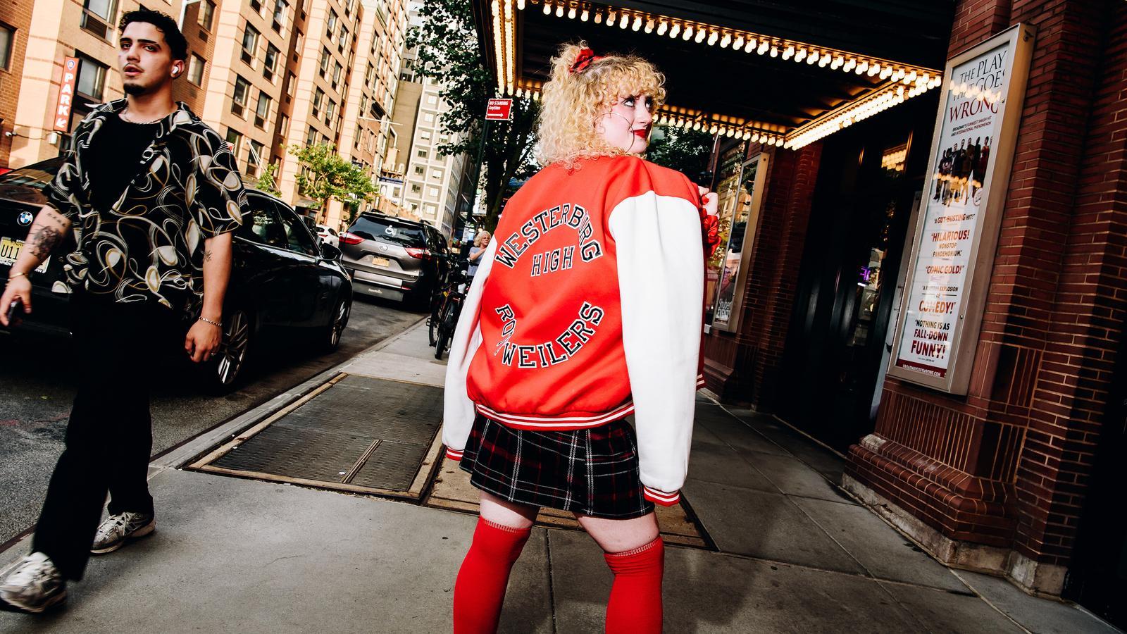 A young woman from New York shows off a varsity jacket outside a theater.
