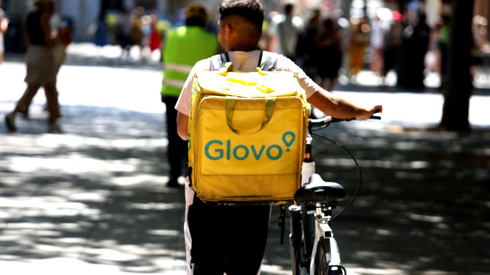 Ein Glovo-Lieferfahrer mit dem Firmenrucksack und seinem Fahrrad in der Innenstadt von Palma.