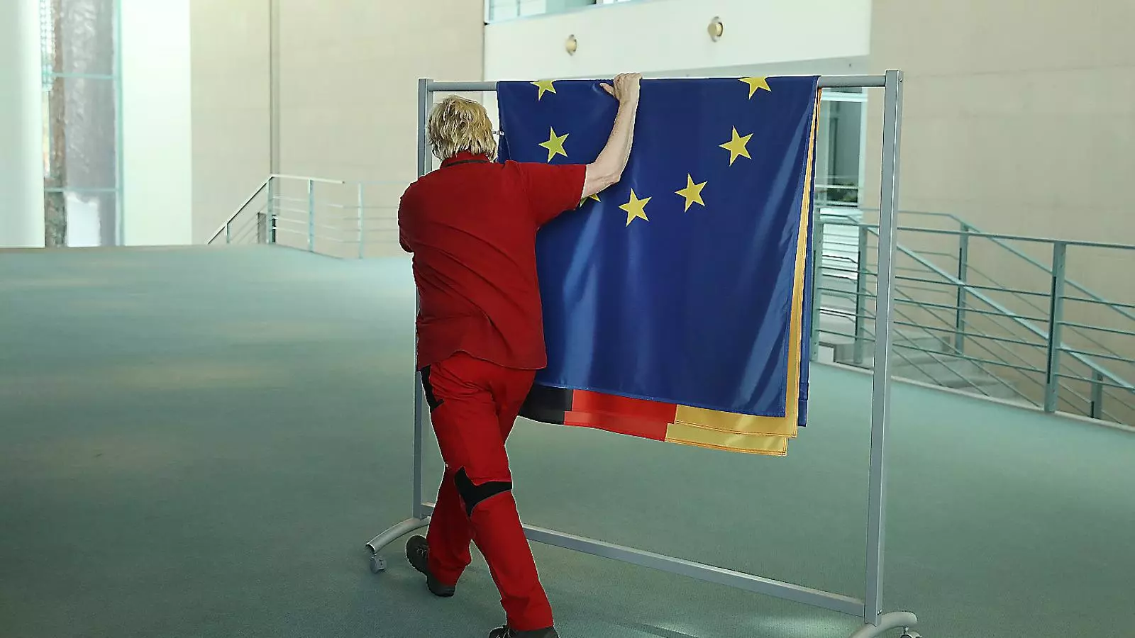 Un treballador preparant les banderes de la UE i d’Alemanya per a un acte oficial.