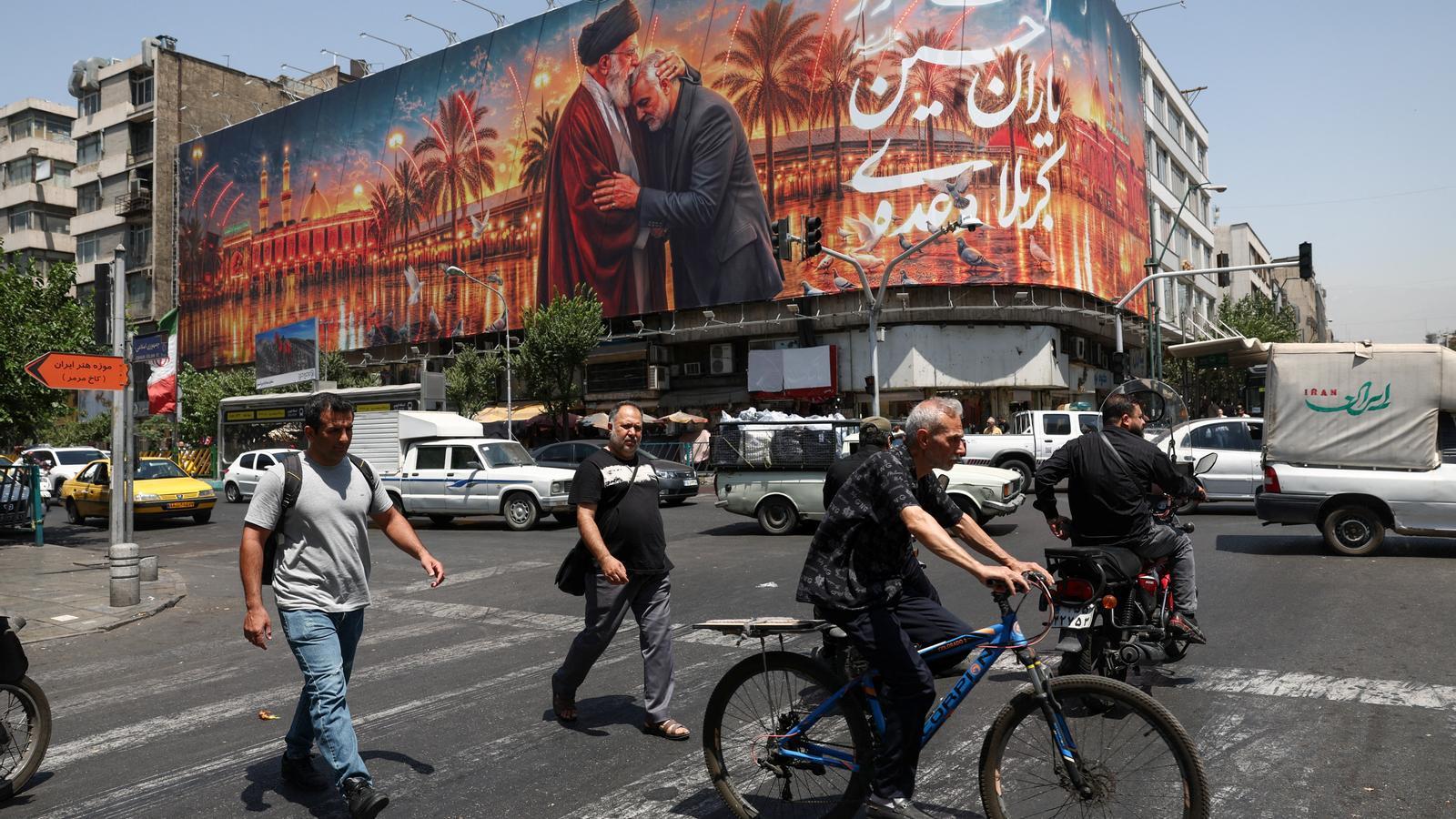 People walk past a billboard with an image depicting the deceased supreme leader of Iran, Ayatollah Ali Khamenei, embracing the deceased Iranian military commander, General Qassem Soleimani, in Tehran