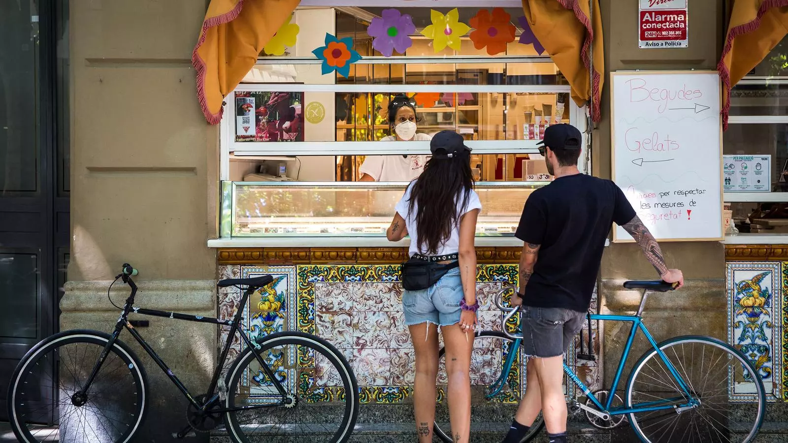 Gelat o orxata? Gelat! De quin gust? Mmm... La Isabel, dependenta de El Tio Che, atèn l'Iris i el Sebastián, veïns del Guinardó, que deixen aparcades un moment les bicis per prendre el seu primer gelat després de la fase més restrictiva del confinament