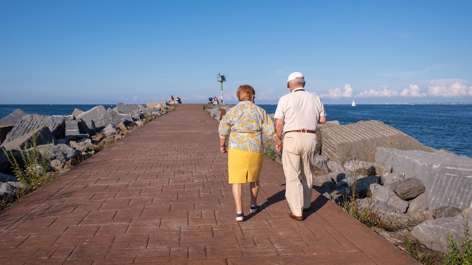 A retired couple walking along the promenade next to the beach.