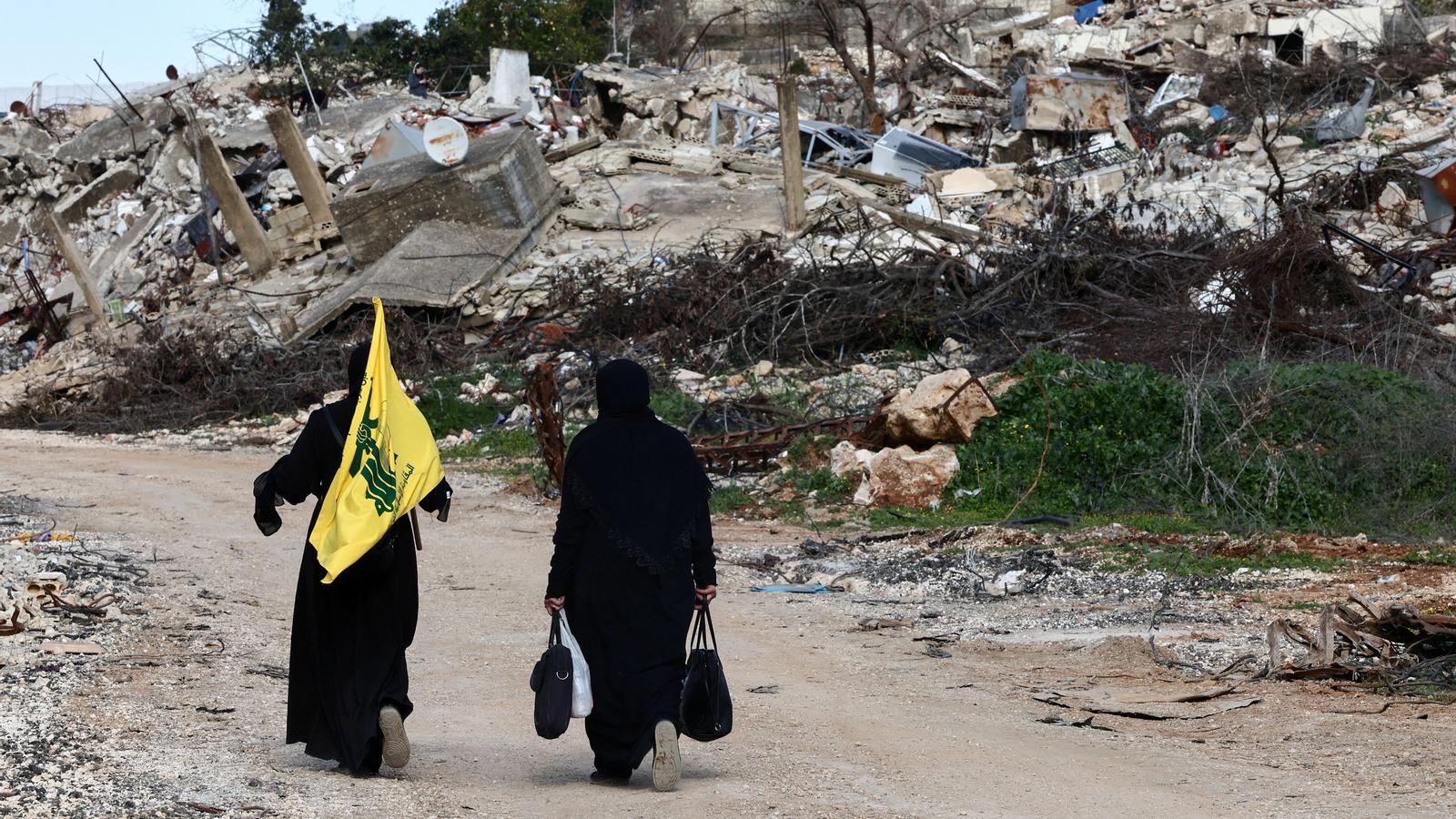 Two women walk among the rubble with the Hezbollah flag in southern Lebanon.