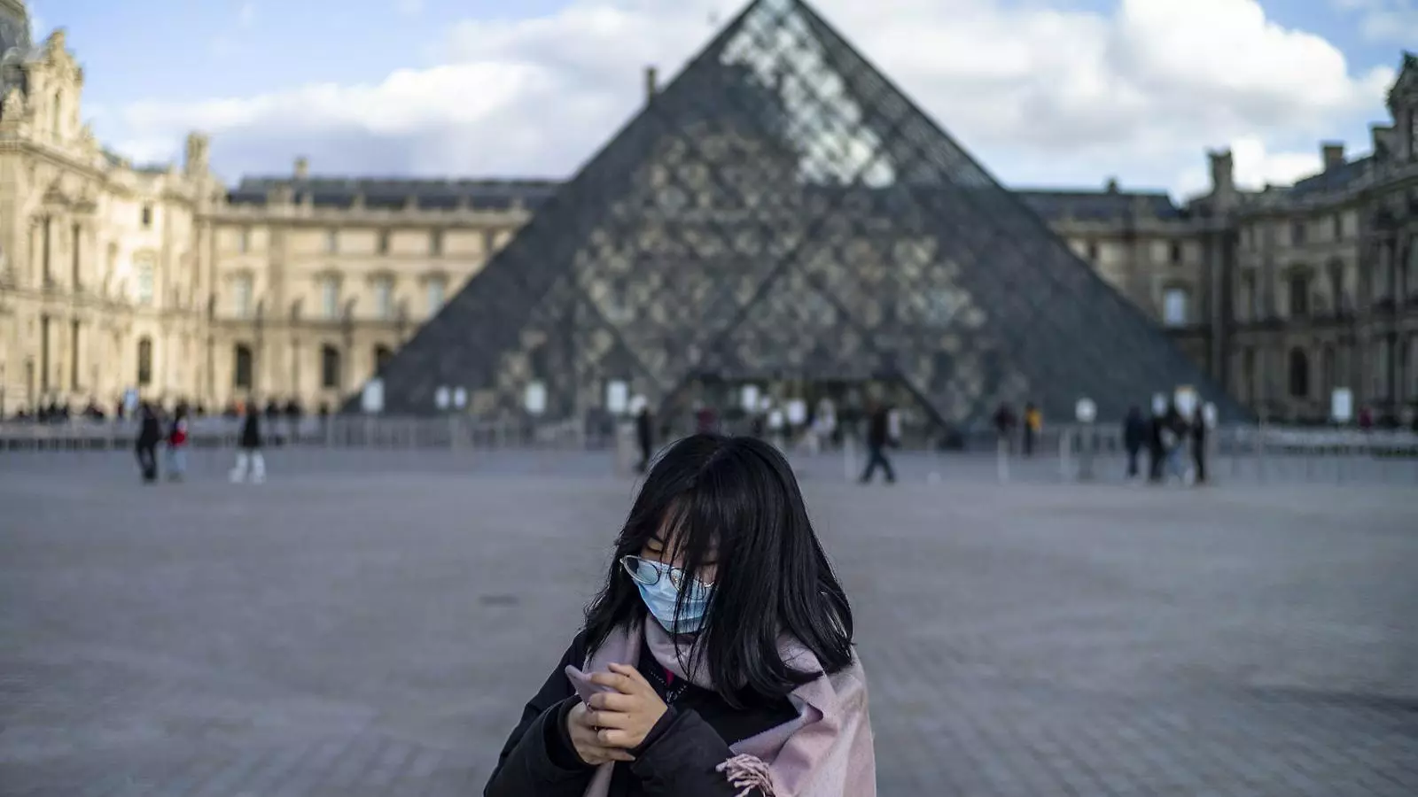 Una jove amb mascareta davant el Louvre, a París, que ha tancat les seves portes.