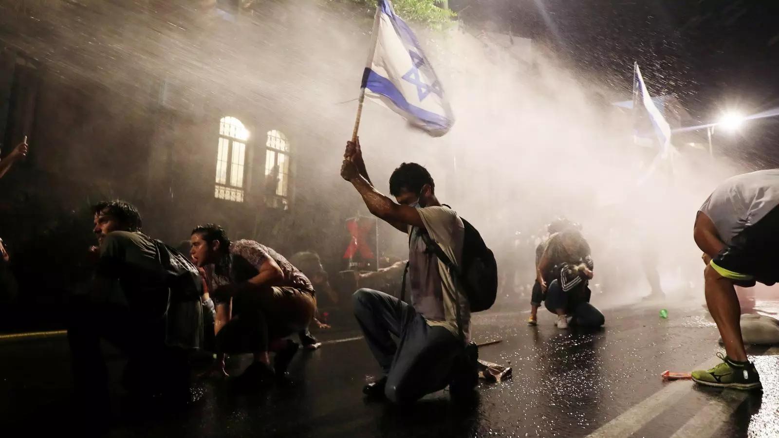 La policia carregant amb canons d'aigua en una manifestació contra Netanyahu, a Tel Aviv, en què un jove manté alçada una bandera israelina