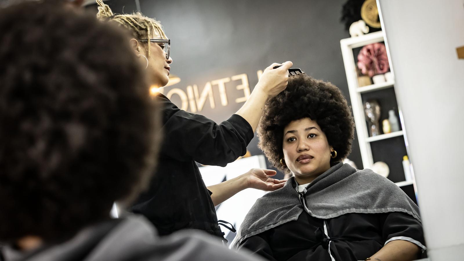 Isabel looks at herself in the mirror while Tamy combs her hair at Iletnic hair salon, in Barcelona.